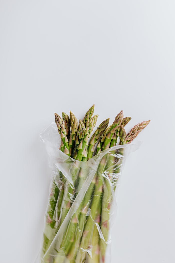 A bunch of fresh green asparagus in a transparent plastic bag on a white background.